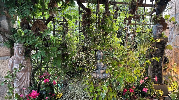 Un jardín con estatuas, abundante follaje y plantas florecientes.