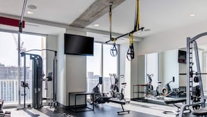 A modern gym with various exercise equipment, large windows, and a flat-screen TV. - Luxury City Center Home (Atlanta)