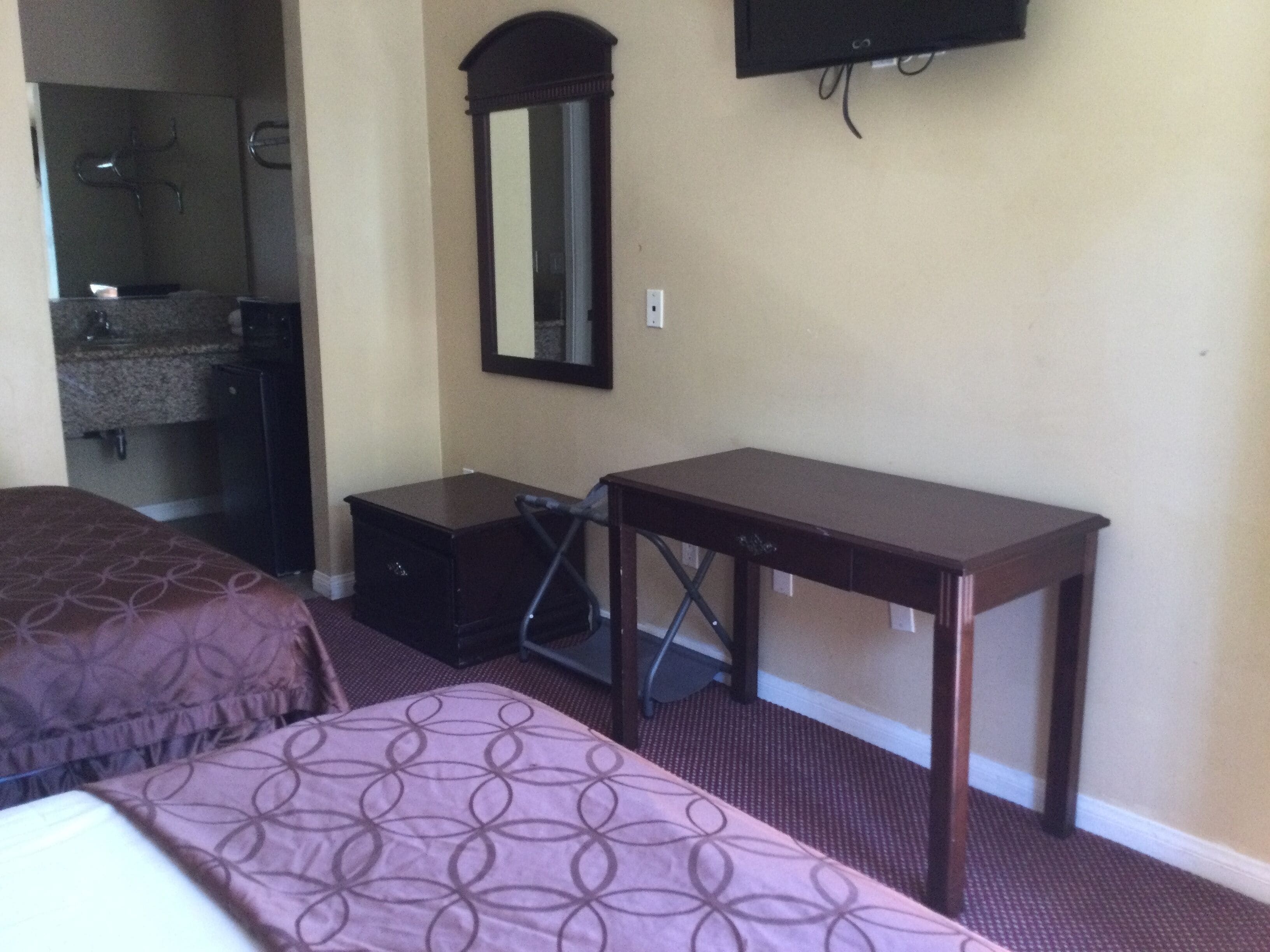 A hotel room with a bed, a dresser, a desk, a mirror, and a television on the wall.
