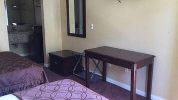 A hotel room with a bed, a dresser, a desk, a mirror, and a television on the wall.