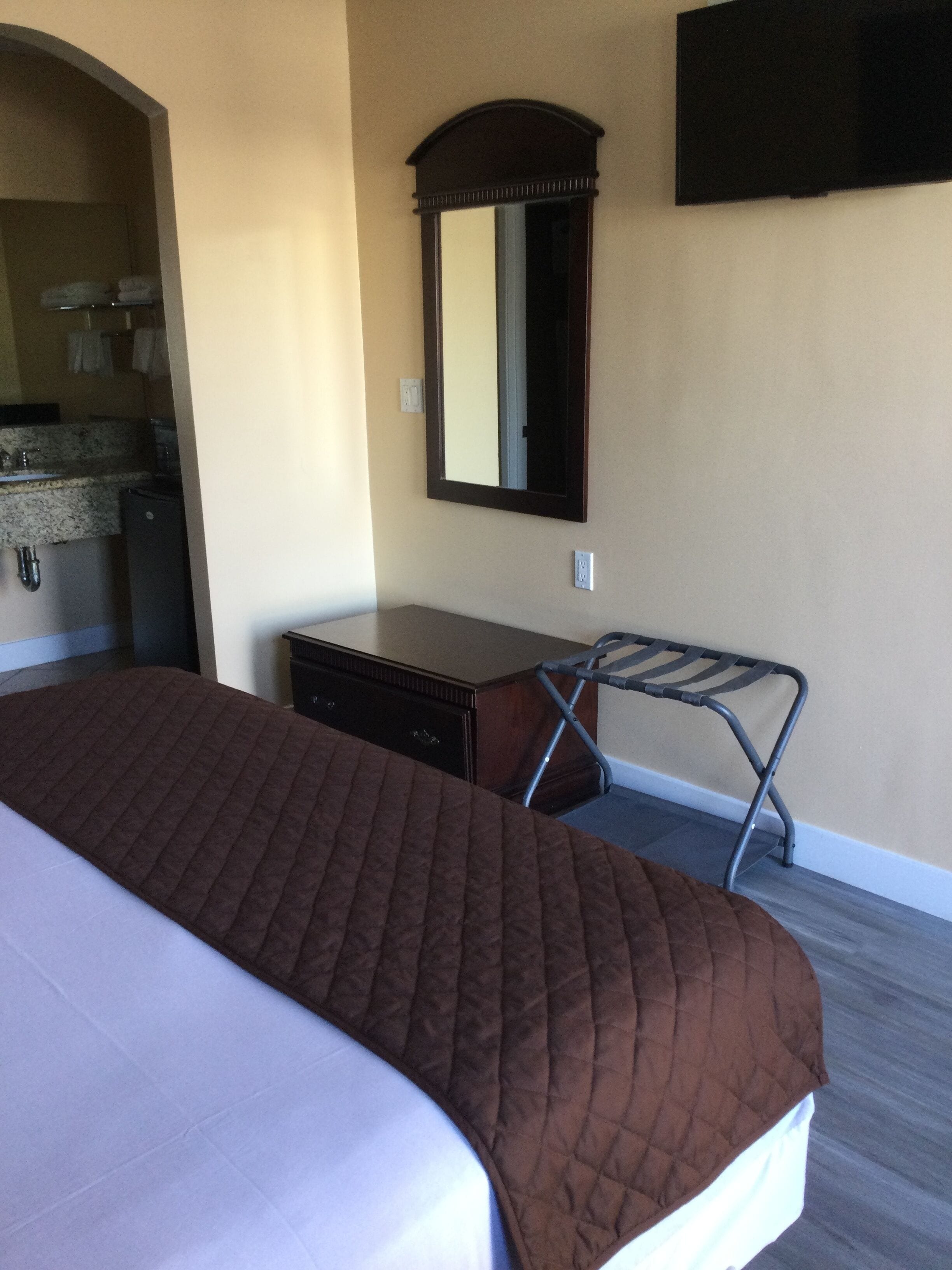 Una camera d'albergo con un letto, una cassettiera, uno specchio e una TV fissata al muro.