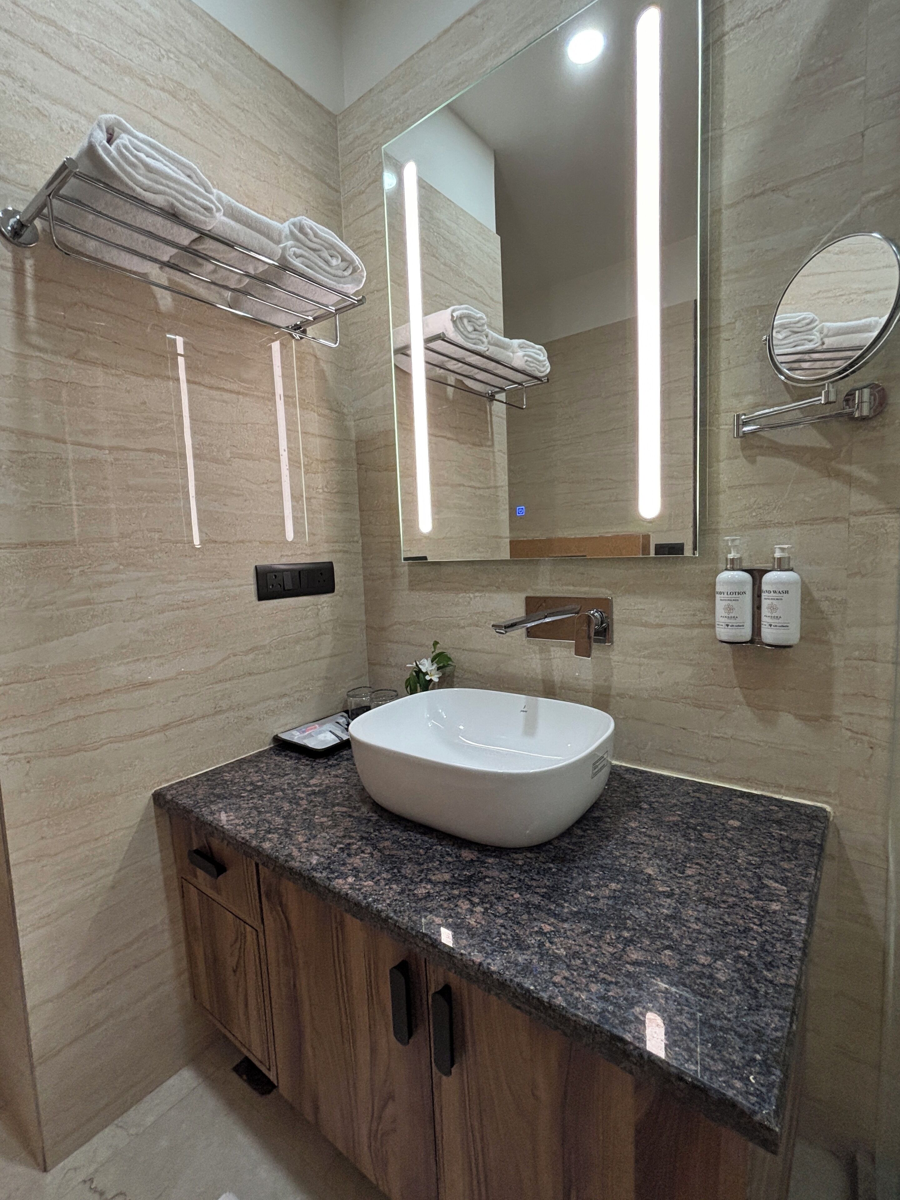 A modern bathroom with a granite countertop, a white sink, wooden cabinets, and a large mirror.
