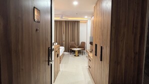 A hallway with wooden paneling, a small table with chairs, and a bed with a curtain. - Anandi Bhawan by Pandora, Vrindavan (Mathura)