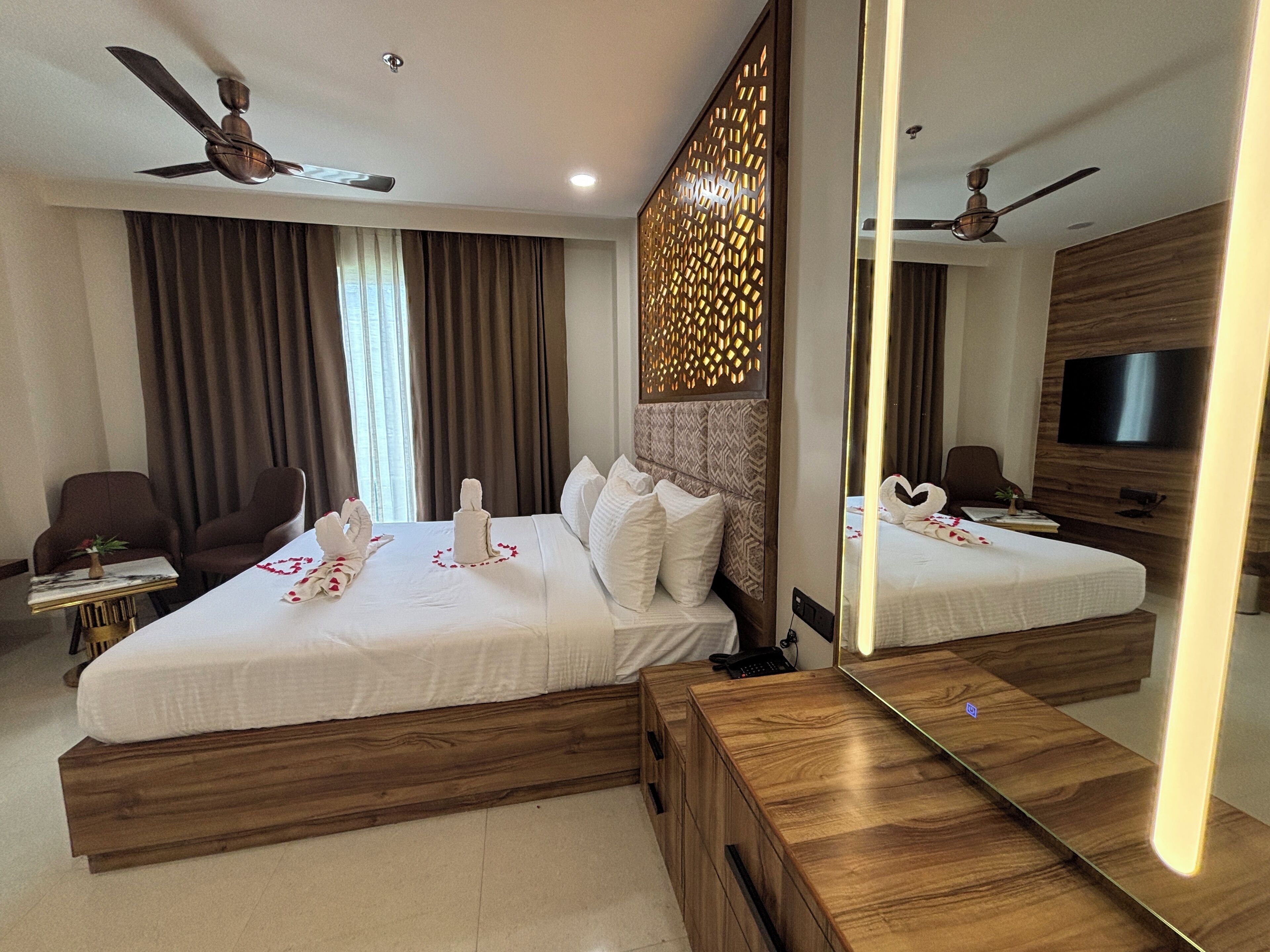 A hotel room with a large bed, a wooden headboard, a desk, a chair, a TV, and a ceiling fan.