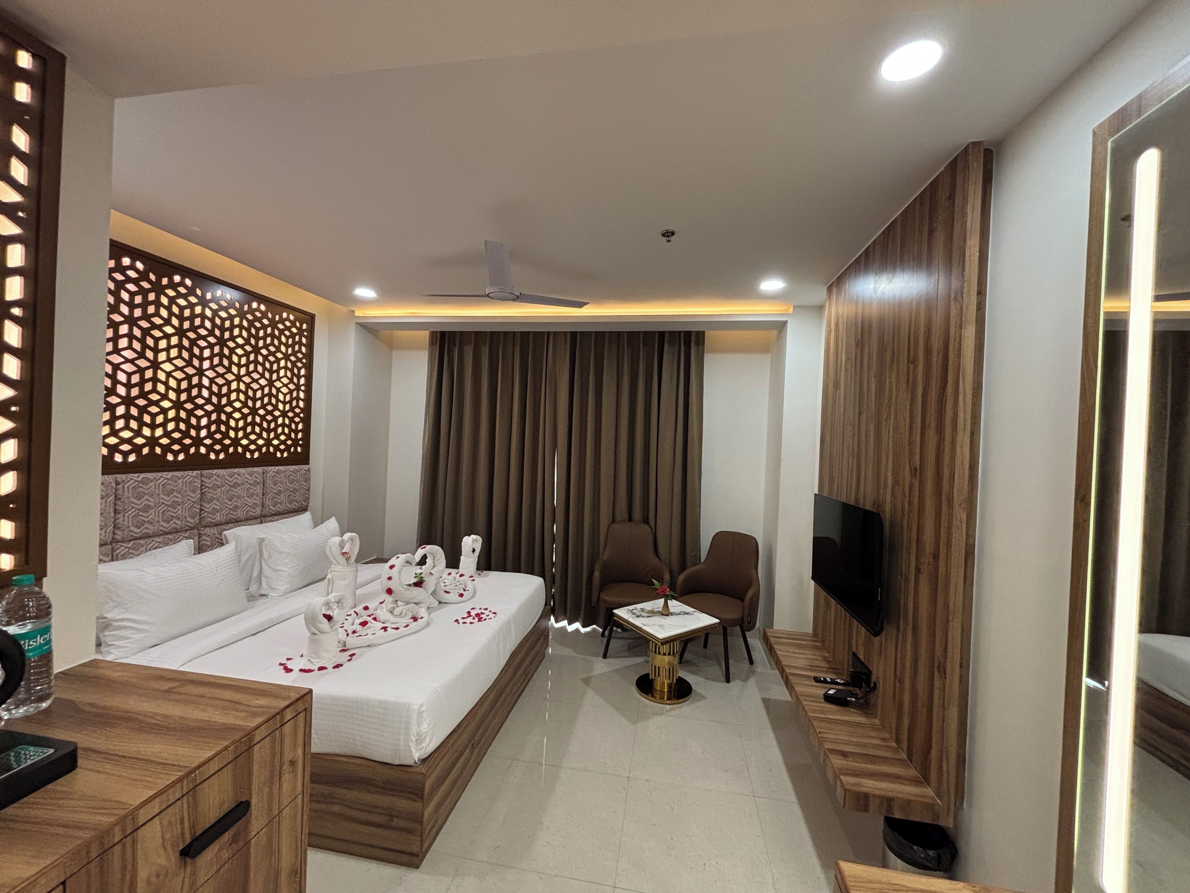 A modern hotel room with a large bed, a TV, a small table, and a seating area.