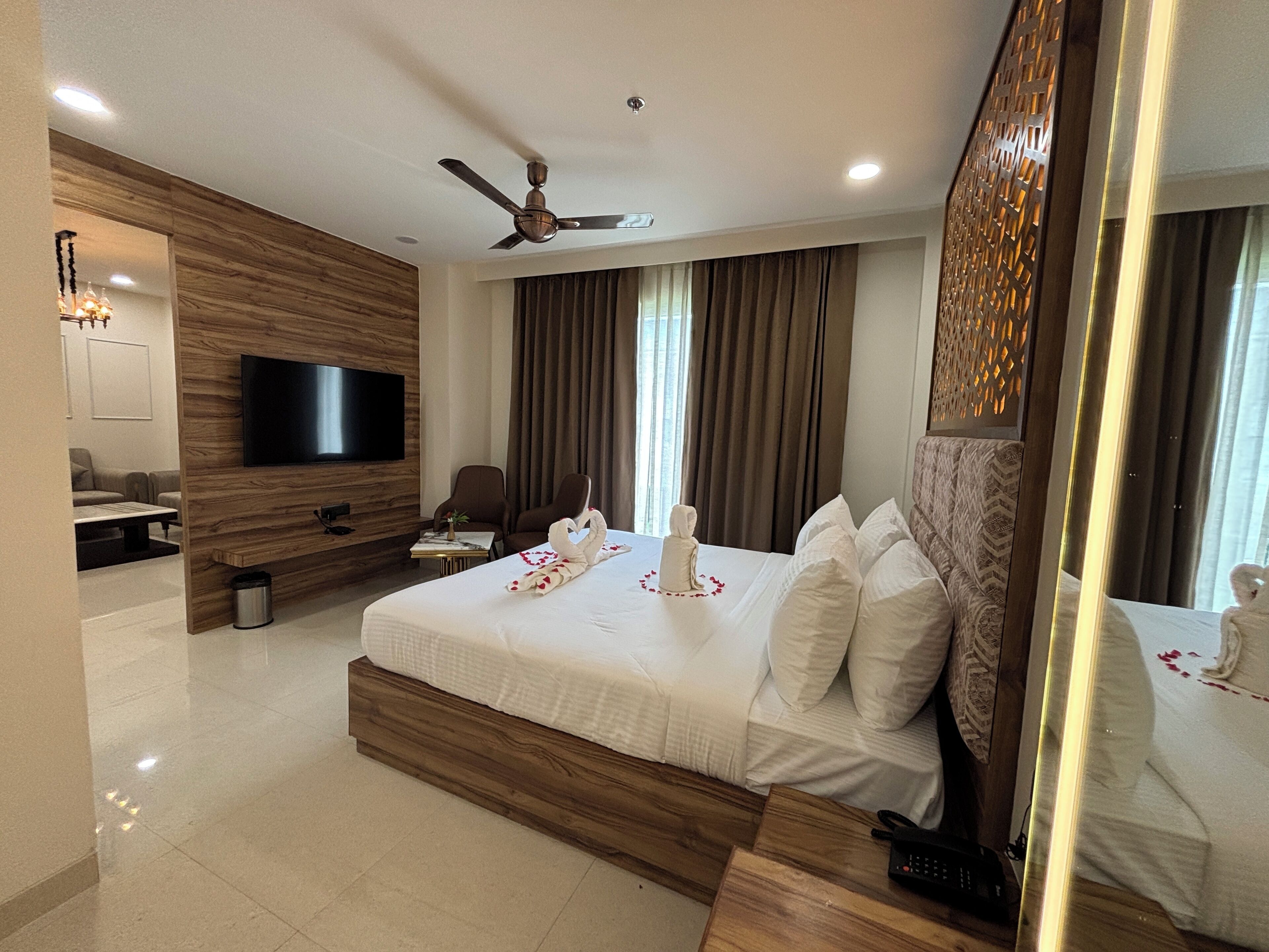 A modern hotel room with a large bed, a flat-screen TV, a ceiling fan, and a seating area with a sofa and chairs.