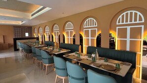 A restaurant with a long table and booths, featuring arched windows and a modern ceiling design. - Anandi Bhawan by Pandora, Vrindavan (Mathura)