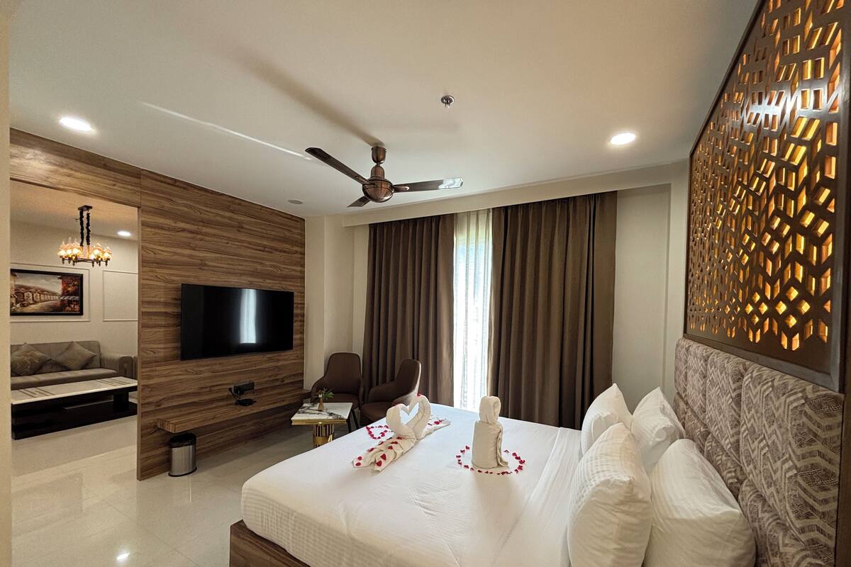 Quarto de hotel moderno com uma cama grande, televisão de tela plana, sofá e mesa de jantar.