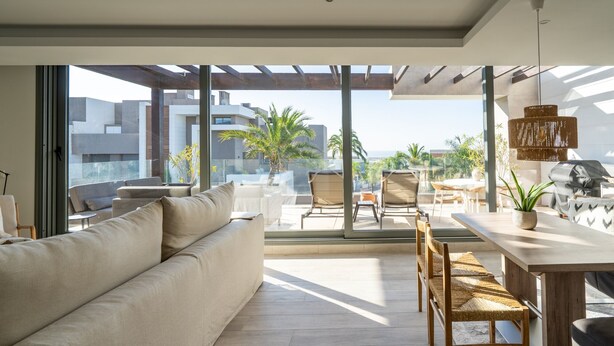 A modern living room with a sofa, dining table, chairs, and a view of the cityscape through large windows.