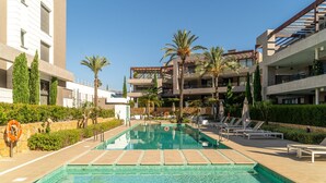 A swimming pool with lounge chairs and palm trees, surrounded by modern buildings.