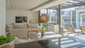 A modern living room with a sofa, coffee table, and chairs. There is a large window with a view of buildings.