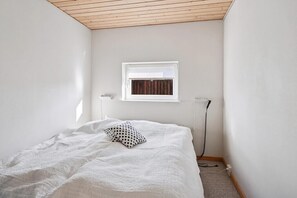 A bedroom with a bed, a window, a wall-mounted heater, and a power outlet.