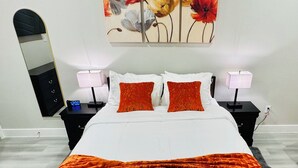 A bedroom with a bed, two bedside tables, a nightstand, a wall clock, and a floral painting.