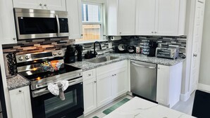 A modern kitchen with white cabinets, stainless steel appliances, a granite countertop, and a view of the outdoors.