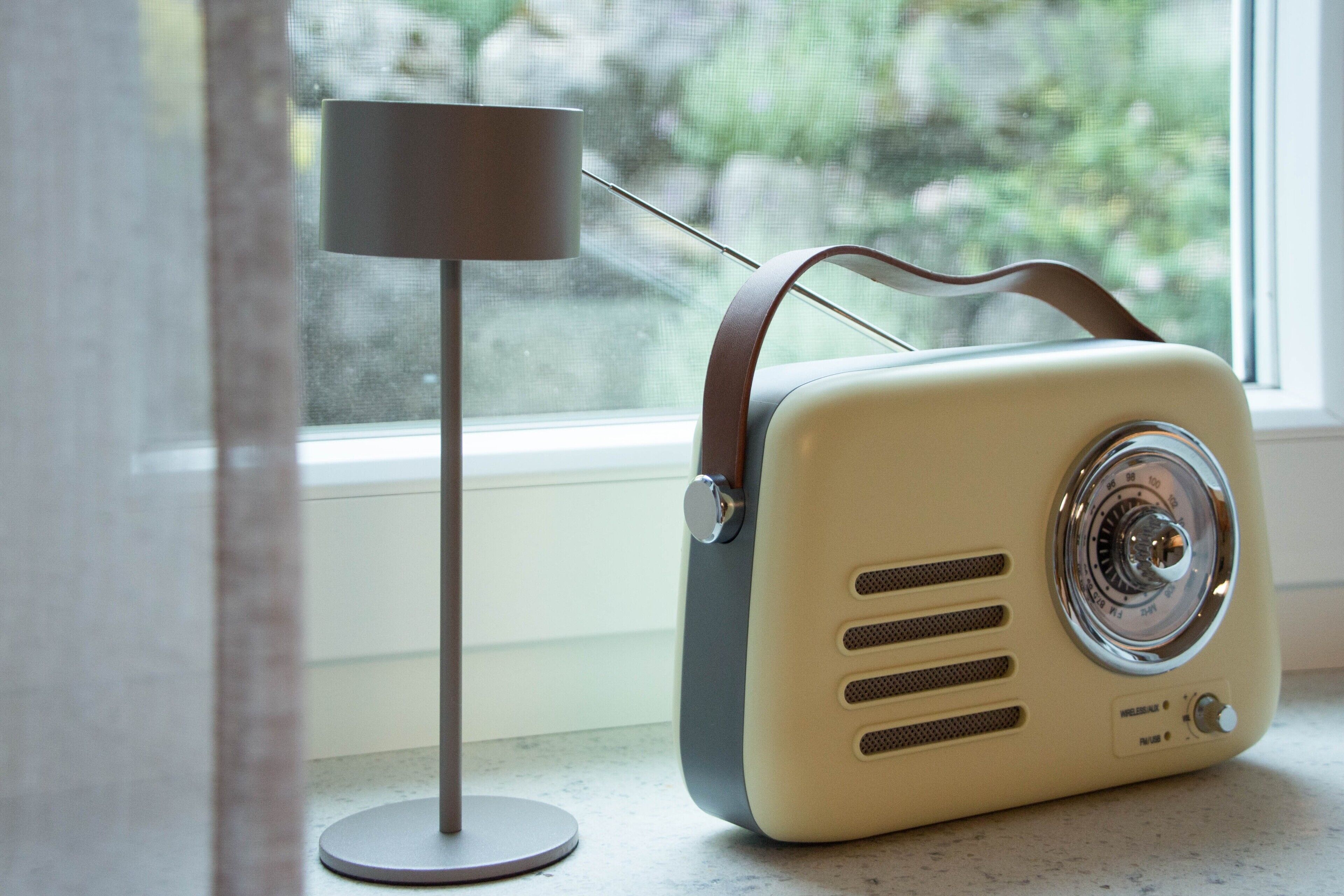 Une vieille radio dotée d’une poignée, une lampe et une fenêtre donnant sur un paysage verdoyant.