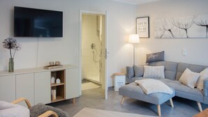 Un salon moderne avec un canapé gris, un téléviseur à écran plat, une bibliothèque et un espace douche.