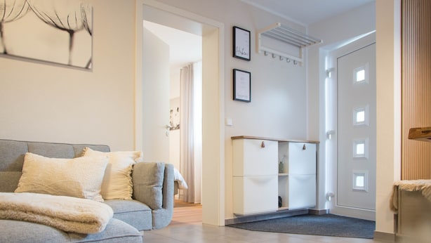 Un salon moderne avec un canapé gris, un meuble blanc et une porte donnant sur une autre pièce.