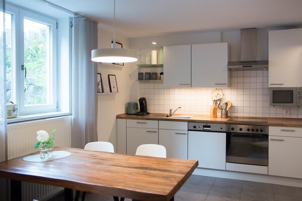 Een moderne keuken met witte kasten, een houten eettafel en een inbouwoven.