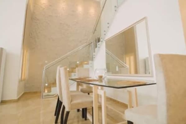 Un comedor moderno con una mesa y sillas de vidrio, una escalera y un espejo grande.