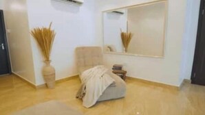 A room with a beige sofa, a large mirror, and a vase with dried plants. - Luxurious 4-Bedroom Serviced Penthouse – The Pearls, Ikoyi (Lagos)