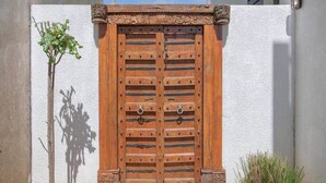 Een houten dubbele deur met decoratieve bovenkant, voor een witte muur.