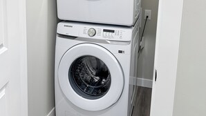 A stacked washer and dryer unit in a laundry room with a white wall and wooden flooring. - Beautiful Cozy Spacious Suite (Calgary)
