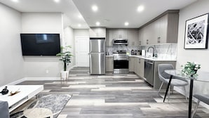 A modern kitchen with stainless steel appliances, a dining area with a glass table, and a living room with a flat-screen TV. - Beautiful Cozy Spacious Suite (Calgary)
