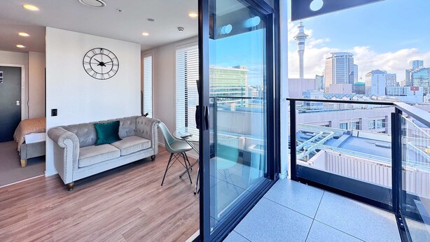 Un salon moderne avec un canapé, une horloge et une vue sur la ville, grâce à de grandes fenêtres.