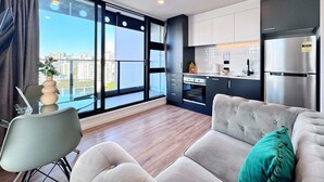 Un appartement moderne comprenant un salon, une kitchenette et de grandes fenêtres offrant une vue sur la ville.
