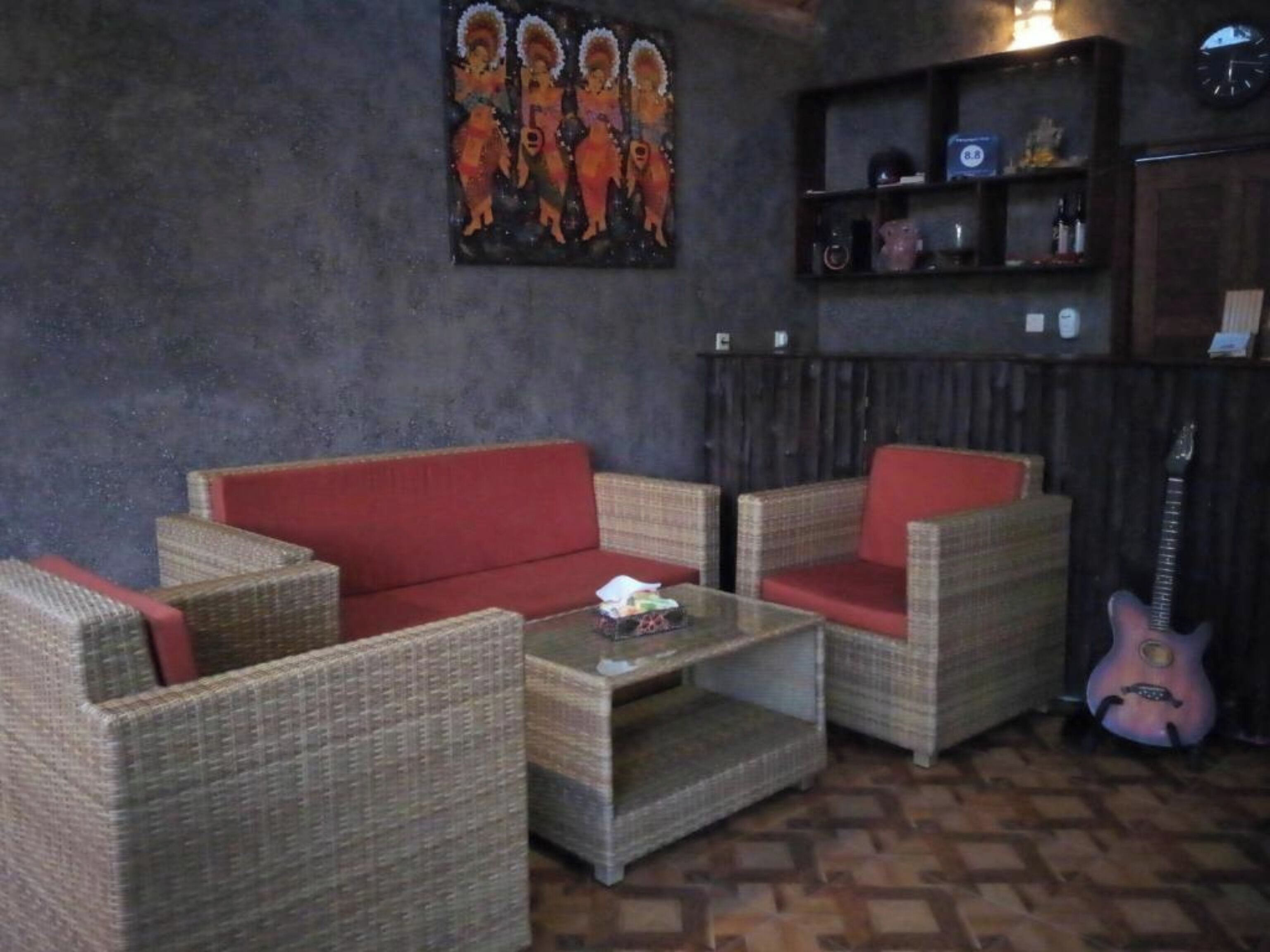 Ein Zimmer mit Korbmöbeln, einem roten Sofa, einem Glastisch und einer Gitarre.