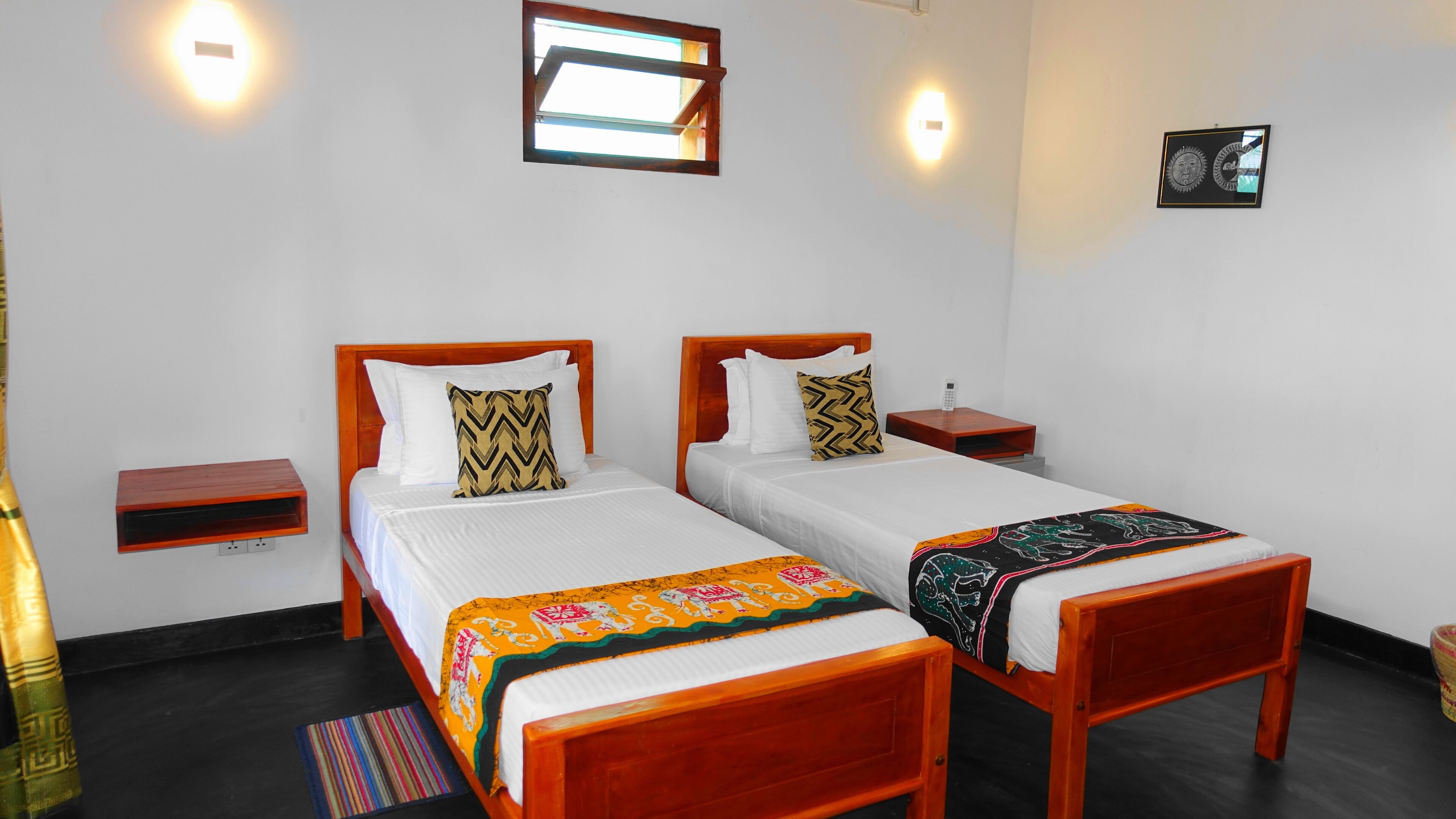 Quarto de hotel com duas camas de madeira, roupa de cama branca e uma pequena mesa de cabeceira com telefone.