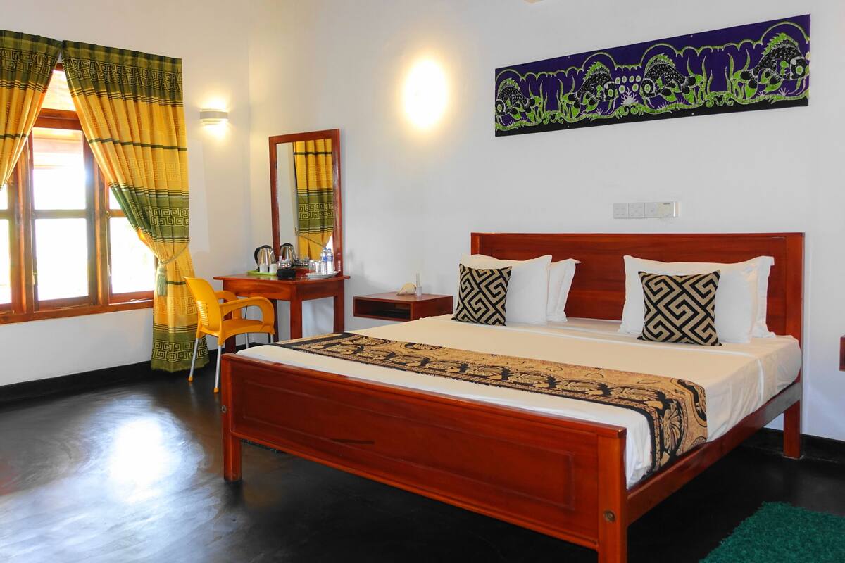 A hotel room with a wooden bed, a desk with a chair, a mirror, and a window with curtains.