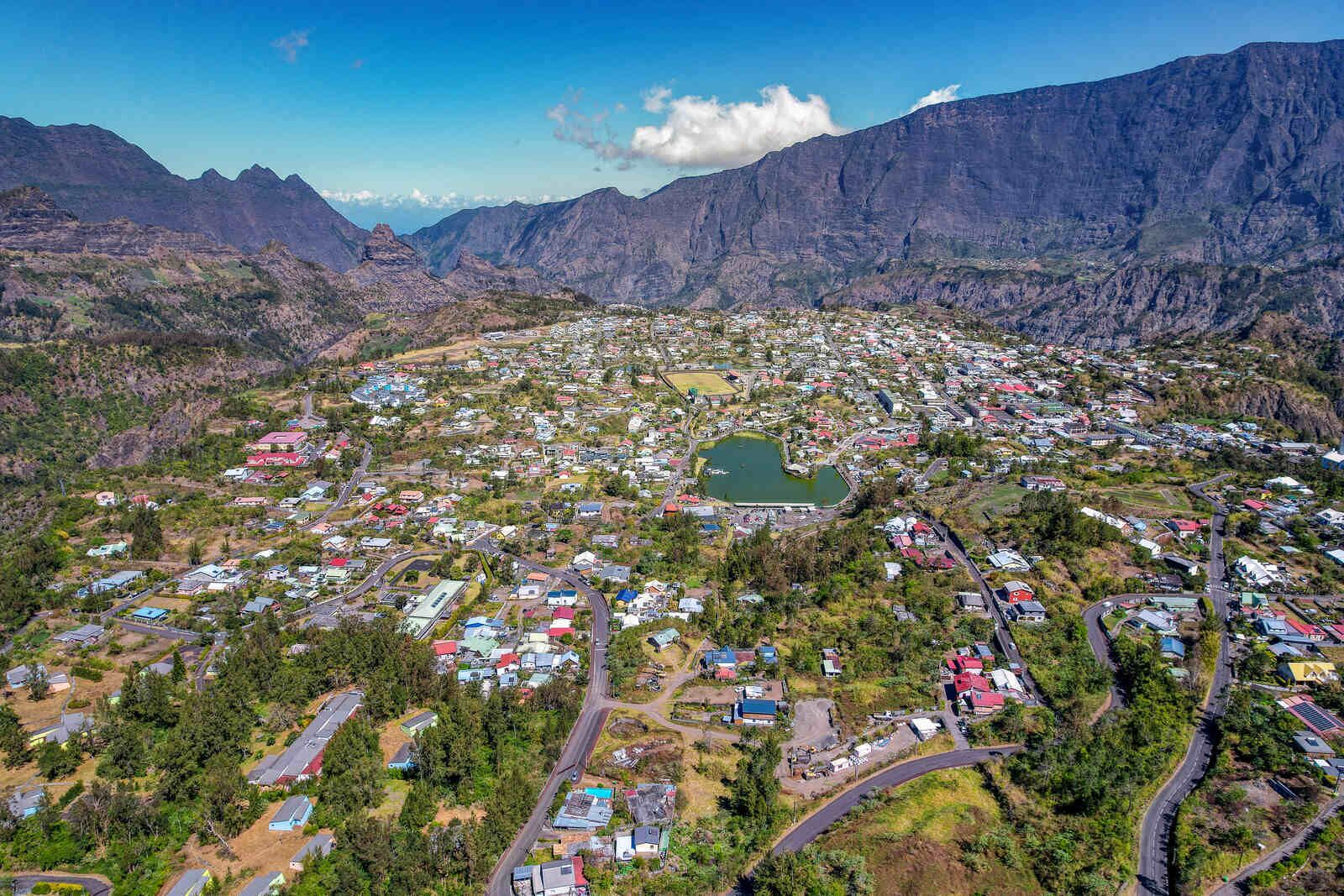 An aerial view of a town with a central lake, surrounded by mountains.