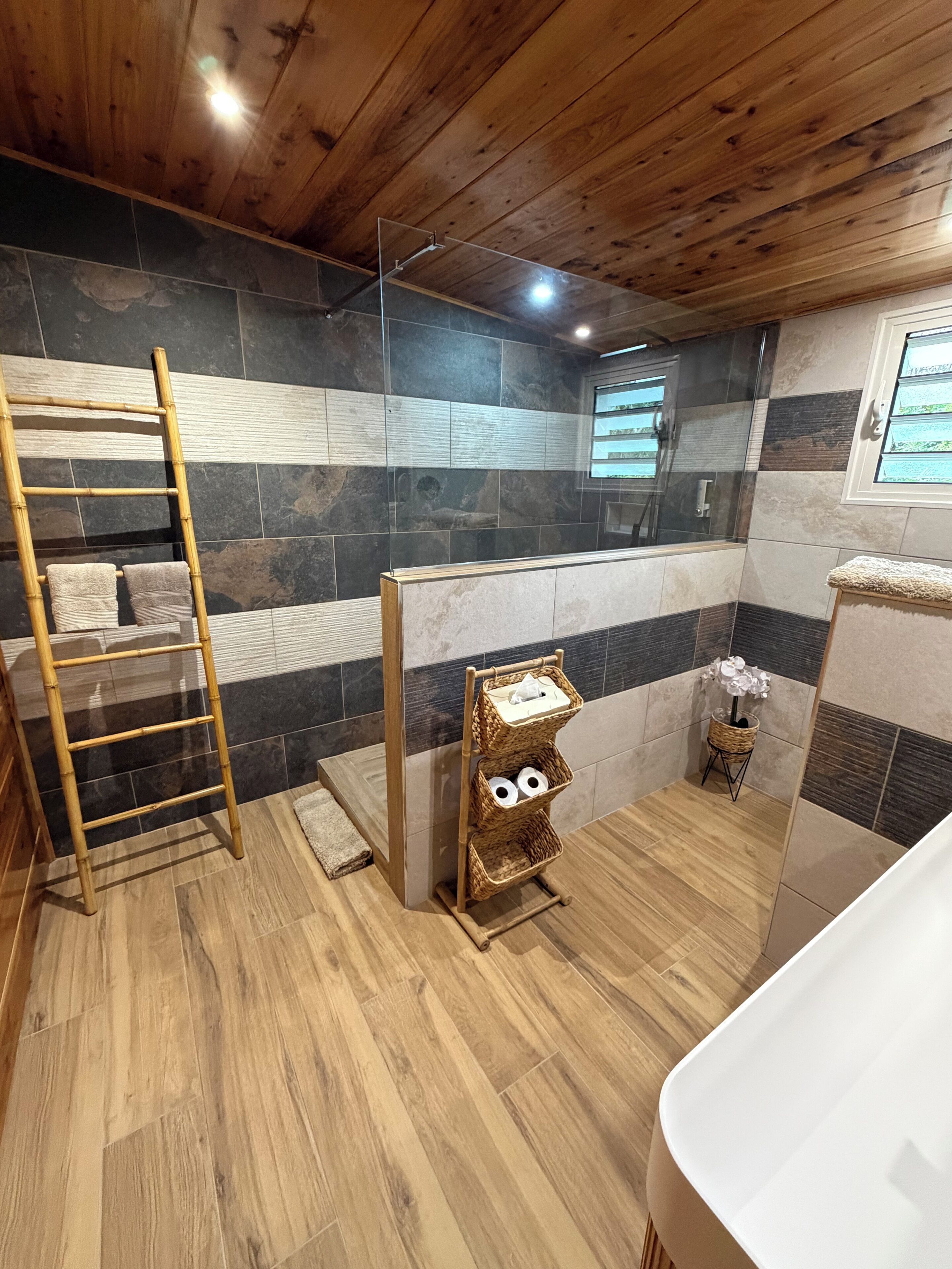 A bathroom with a wooden ceiling, a bamboo ladder, a wall-mounted toilet paper holder, and a bathtub.
