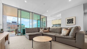 Ein modernes Wohnzimmer mit einem Ecksofa, einem runden Couchtisch und Blick auf eine Skyline durch große Glasfenster.