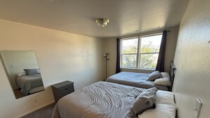 Ein Schlafzimmer mit zwei Betten, einem kleinen Nachttisch, einem Spiegel und einem Fenster mit Vorhängen.