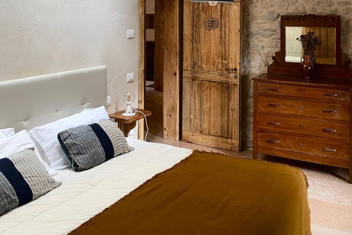 Quarto com cama, cómoda de madeira e parede de pedra.