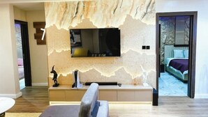 A modern living room with a large flat-screen TV mounted on a textured wall, a sofa, and a coffee table. - 🏡 Luxury 2 bedroom apartment (Lagos)