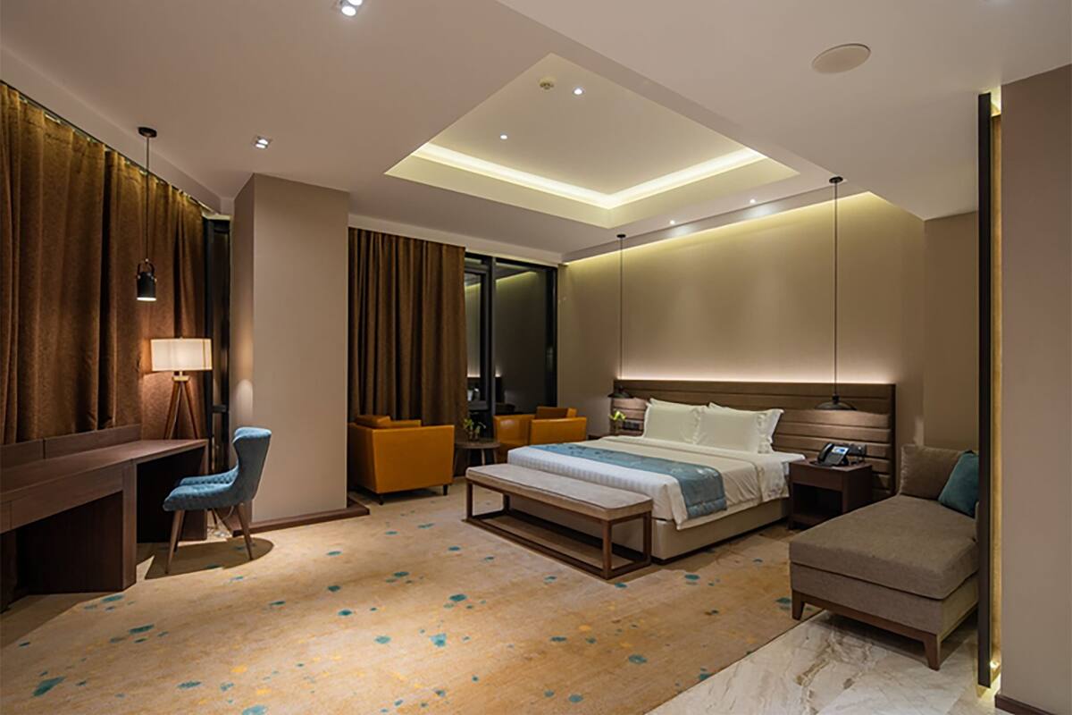 A modern hotel room with a large bed, a desk, a chair, and a sofa.