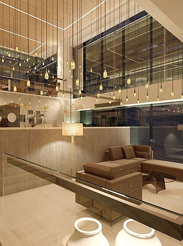 A modern interior with a glass railing, a sofa, and hanging light fixtures.