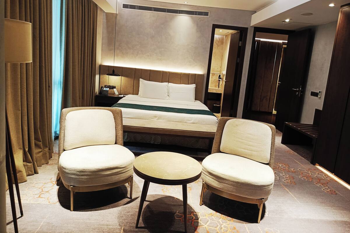 A hotel room with a bed, two armchairs, a small table, a nightstand, and a lamp.