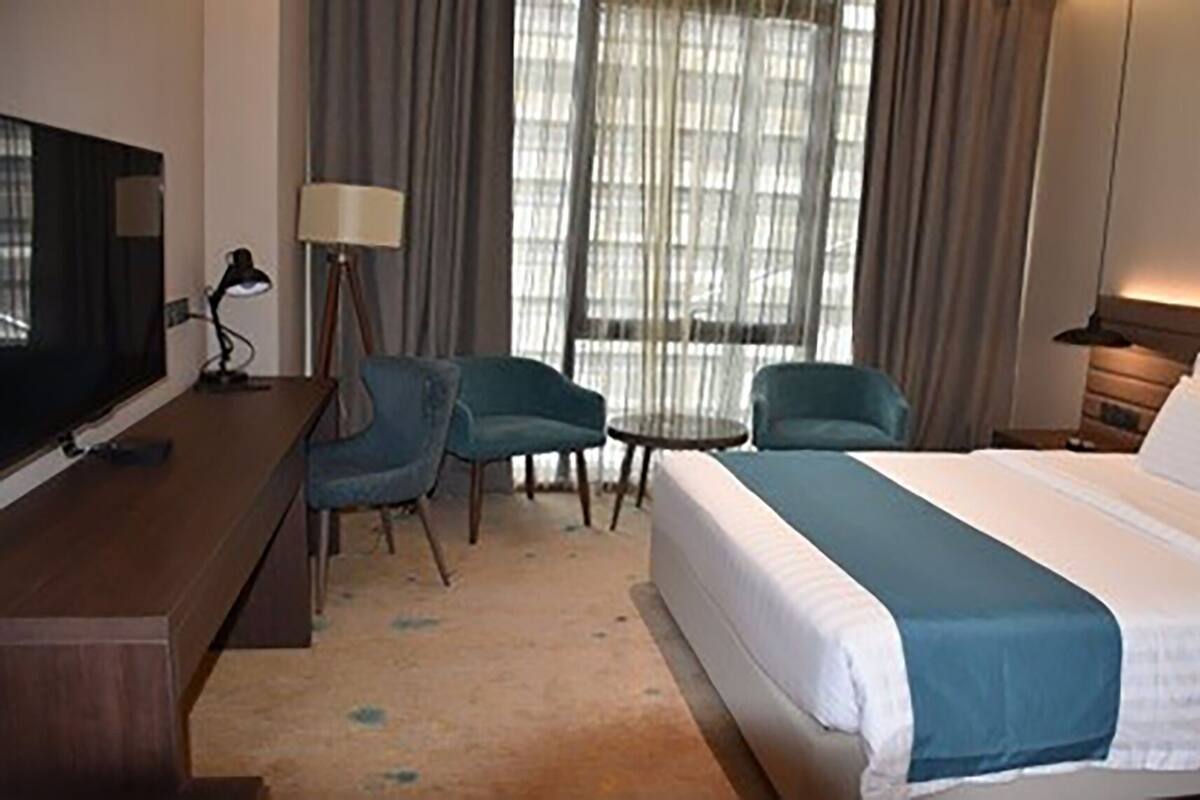 A hotel room with a bed, two armchairs, a small table, a TV, and a lamp.