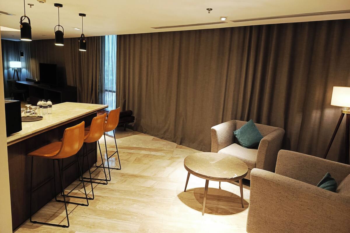 A modern hotel room with a wooden bar, two sofas, a round table, and a television.