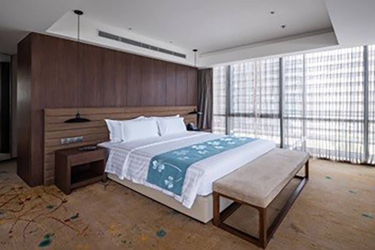 A modern bedroom with a large bed, wooden headboard, bedside tables, and a bench.
