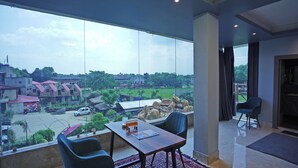Habitación moderna con un ventanal grande que ofrece vistas a una zona residencial y un jardín. Hay una mesa de madera con sillas y una alfombra pequeña en el suelo.