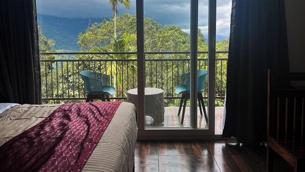 A bedroom with a large sliding glass door leading to a balcony with two chairs and a small table.
