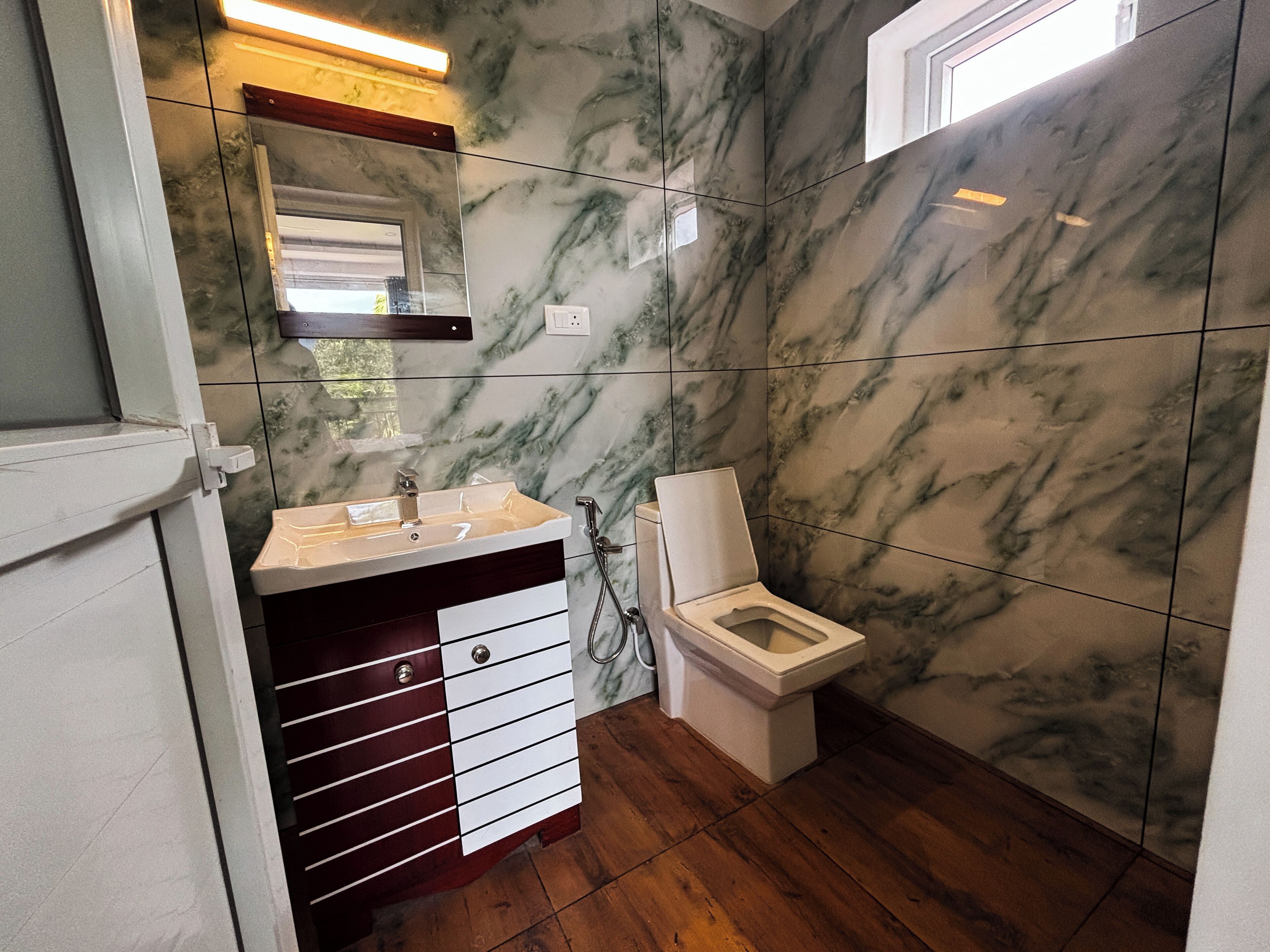 A bathroom with a marble wall, a wooden floor, a sink, a toilet, and a mirror.
