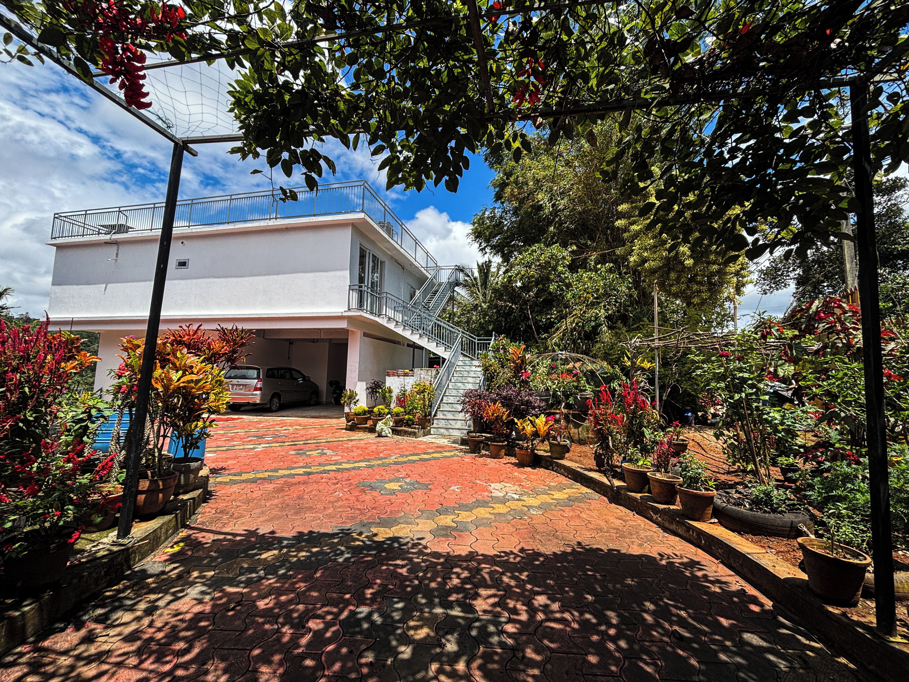 A building with a covered parking area, a staircase leading to a balcony, and a variety of potted plants and flowers.