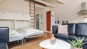 Een compacte leefruimte met stapelbedden, een kitchenette, een zwarte leren bank en een ronde salontafel.