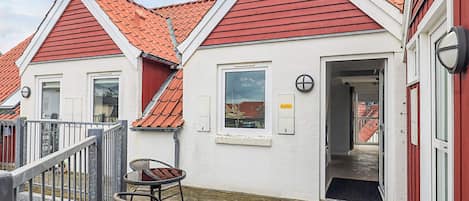 A building with a red roof and white walls, featuring a door, a window, and a small outdoor seating area with a table and chairs.